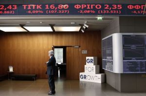 A man stands under an electronic board displaying stock prices in the reception hall of the Athens Stock Exchange in Athens