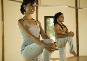 Dos personas realizan una postura de yoga con una sola pierna en el suelo.